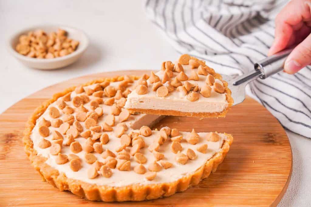 hand lifting slice of peanut butter pie away from remaining pie