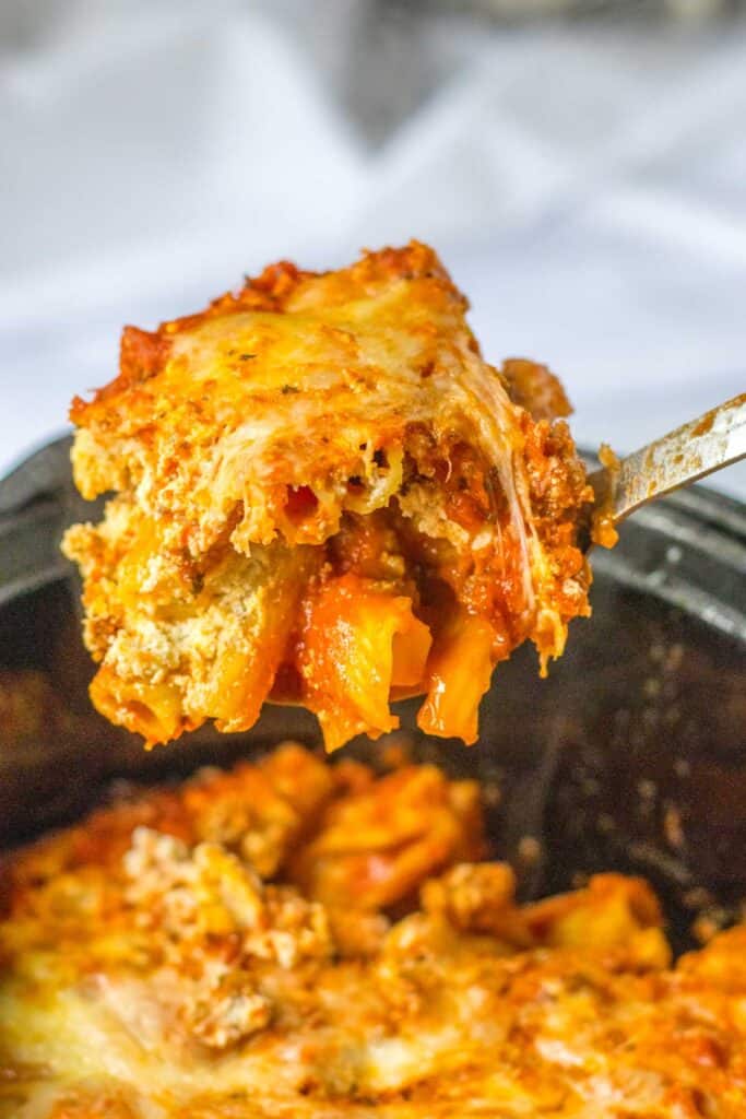 large spoon scooping slow cooker baked ziti out of crock pot