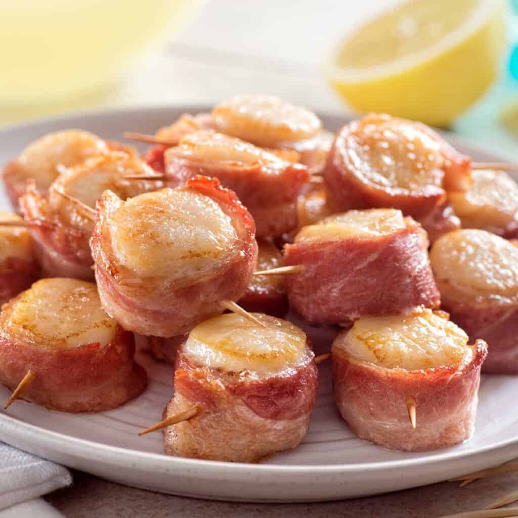 bacon wrapped scallops with lemon in background