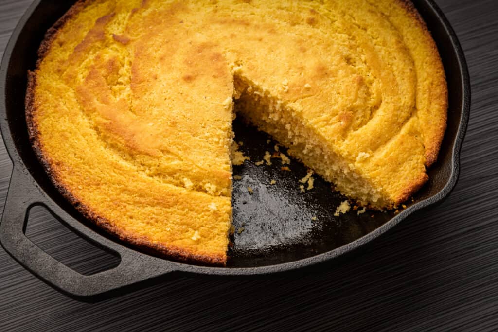 gietijzeren koekenpan met maisbrood en één sneetje verwijderd