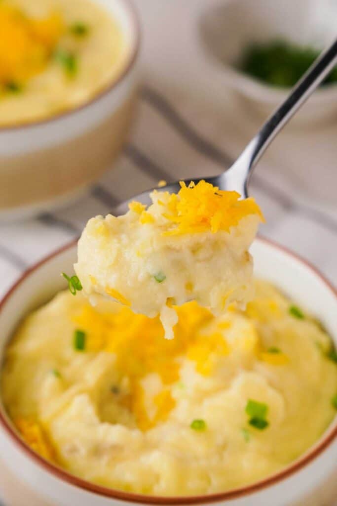 spoonful of cheesy mashed potatoes with bowl in background