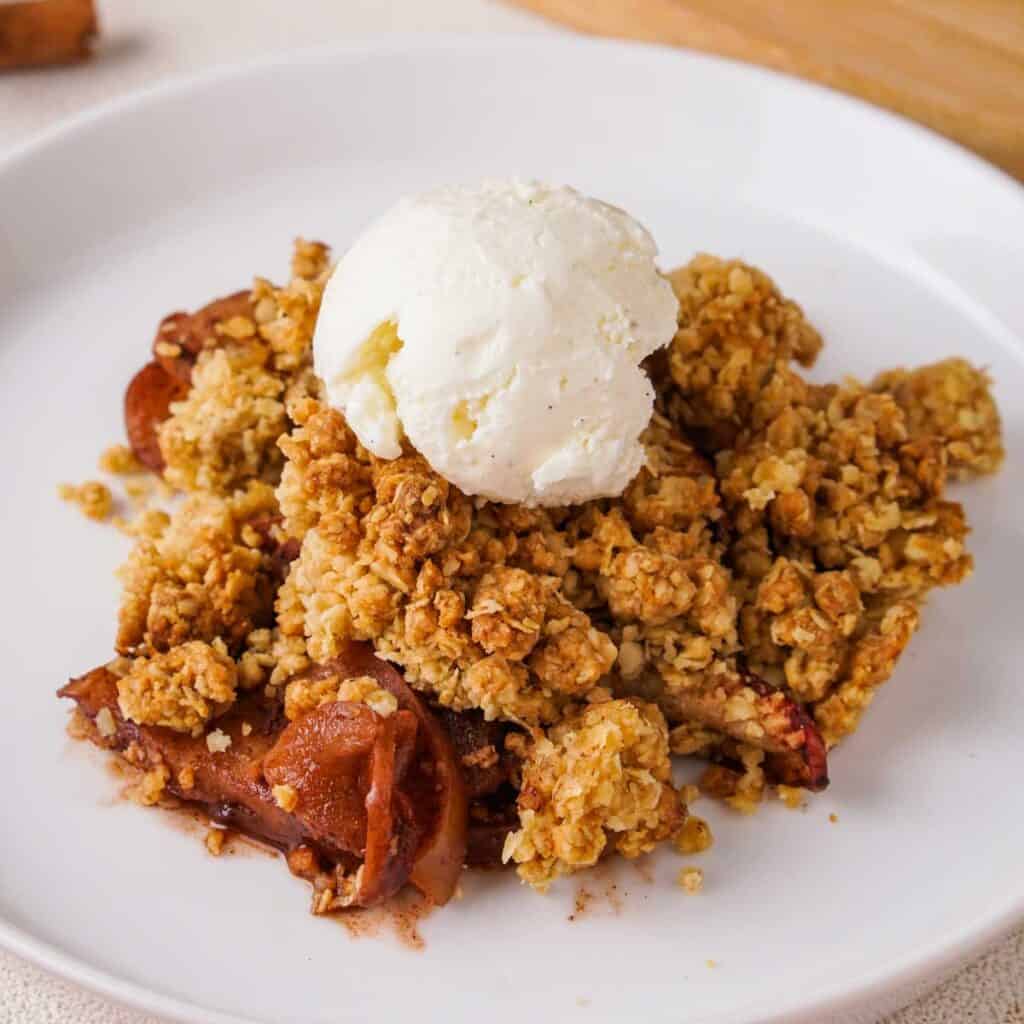 old fashioned apple crisp on white plate with scoop of vanilla ice cream
