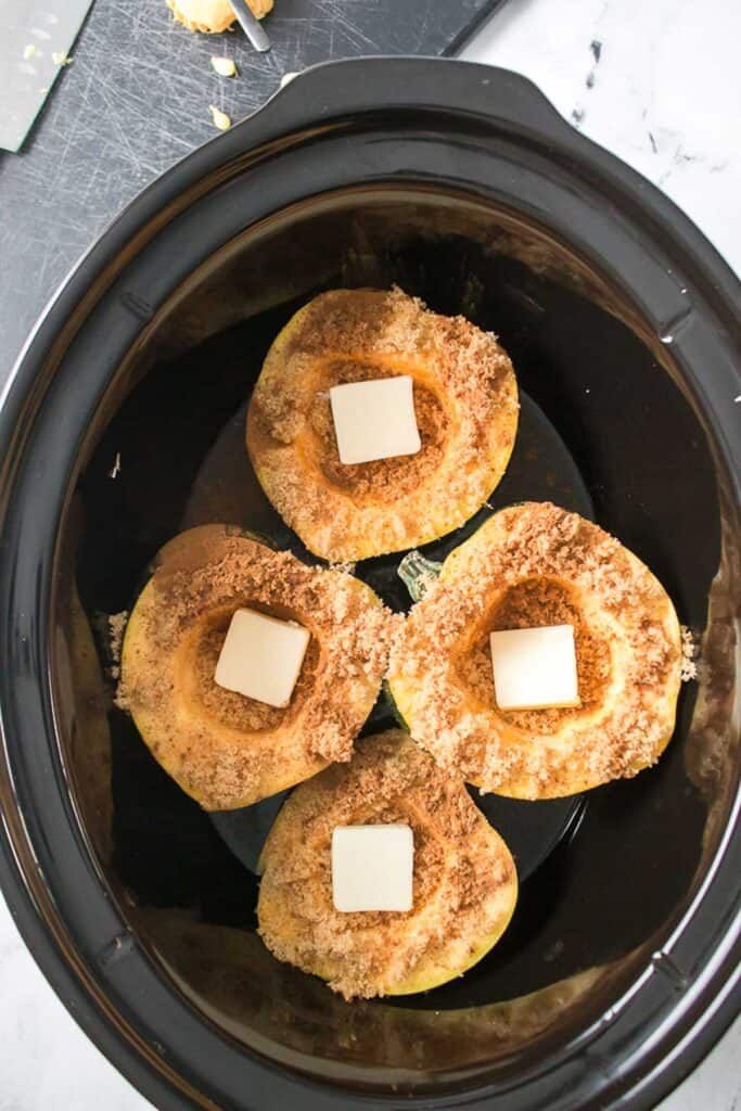 4 acorn squash halves in slow cooker with brown sugar and pats of butter