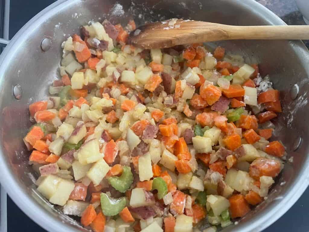 chopped vegetables cooking in pan with wooden spoon