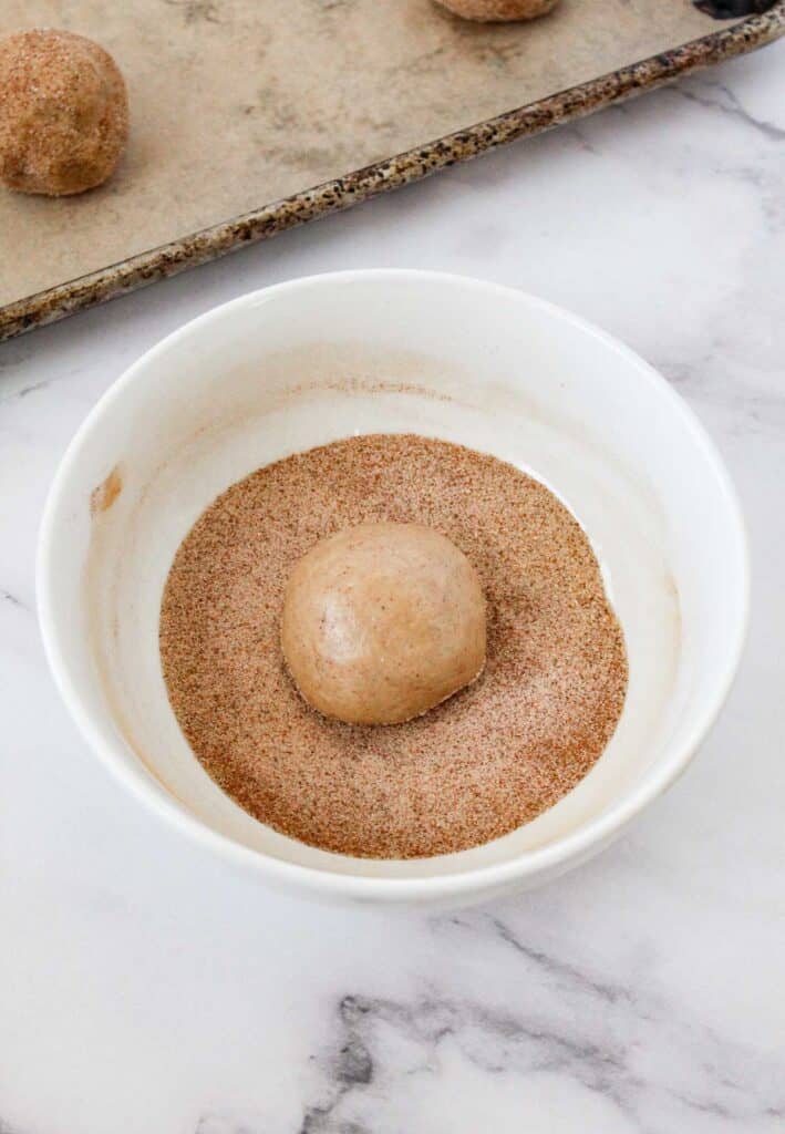 rolling snickerdoodle dough ball in cinnamon sugar