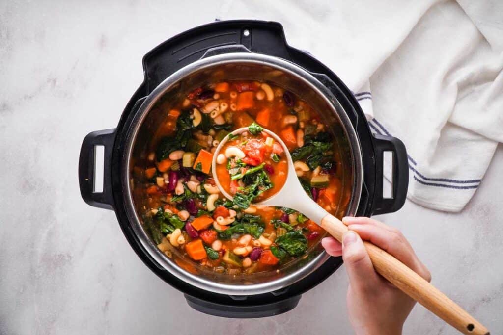 holding ladle full of minestrone over Instant Pot