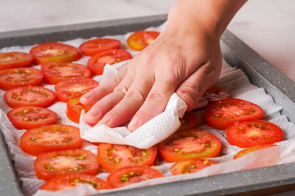 blotting tomato slices with paper towel