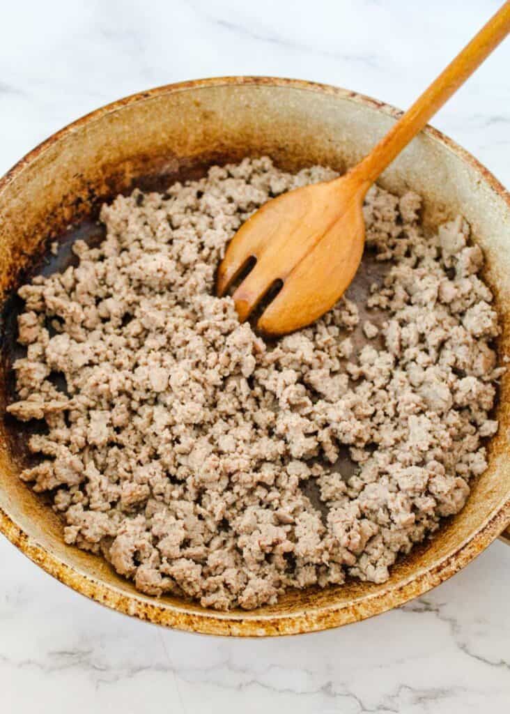 wooden spoon breaking up ground turkey while cooking in a skillet