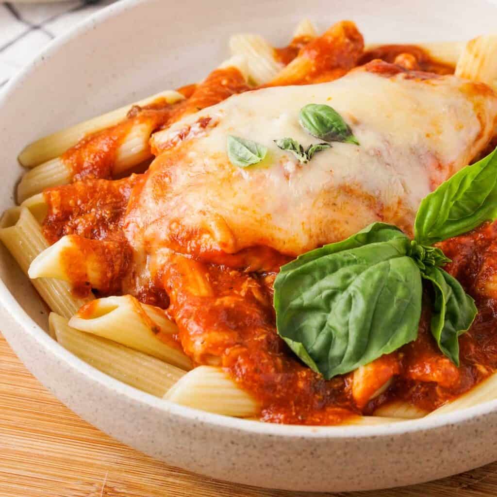 close up of instant pot chicken parmesan in white bowl over penne