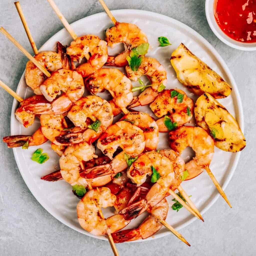 grilled skewered shrimp on white plate with red dipping sauce