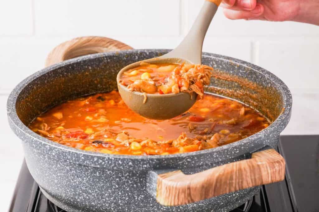 ladle scooping brunswick stew out of a heavy pot