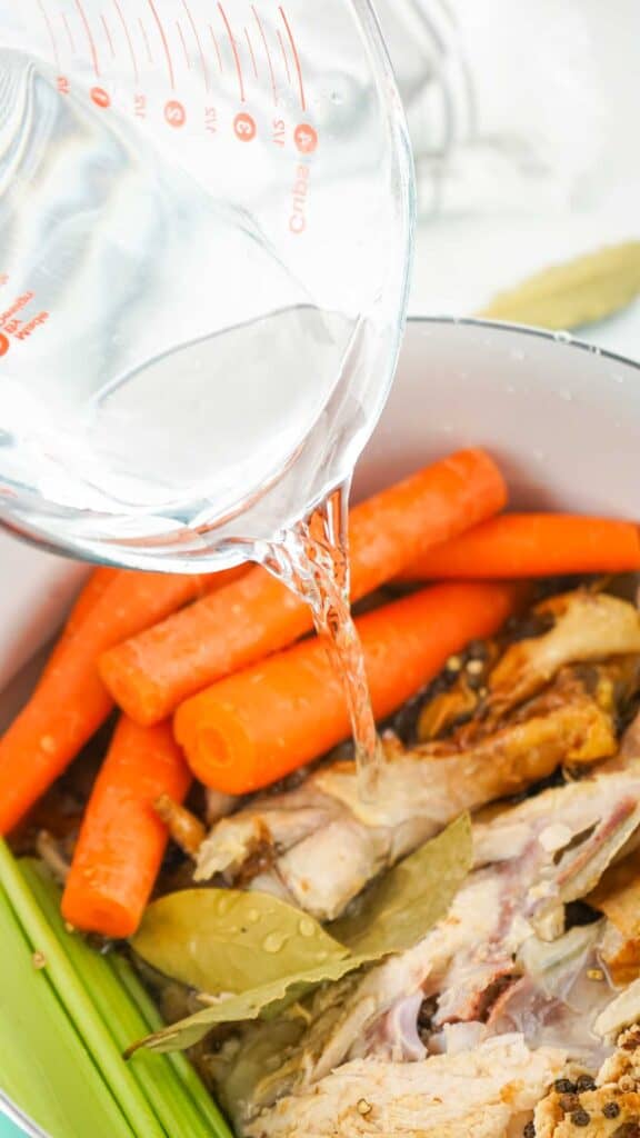 pouring water over chicken, carrots, and celery
