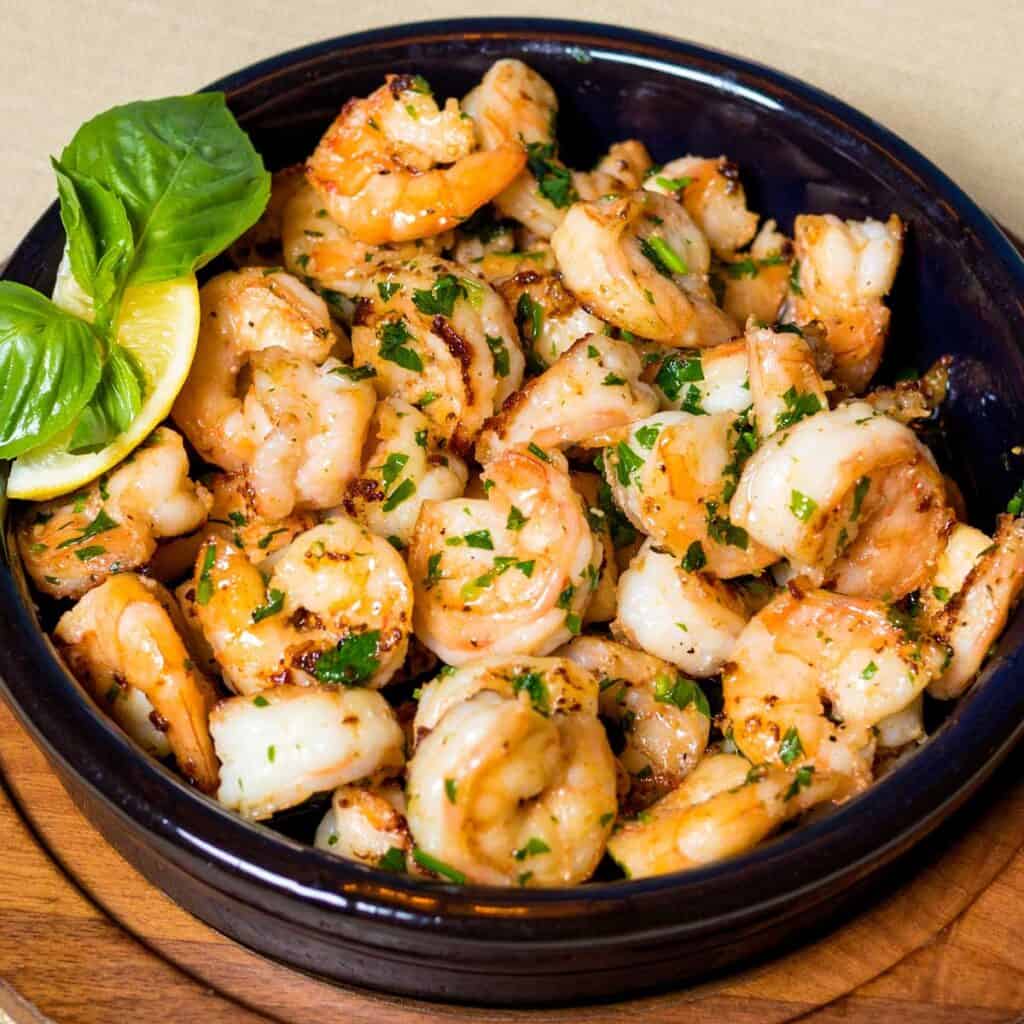 shrimp scampi in black dish with basil and lemon garnish
