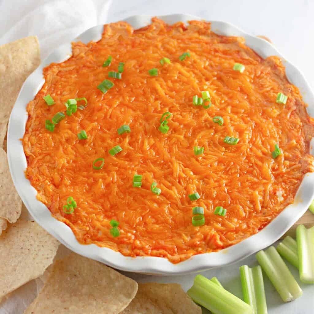 buffalo chicken dip in white baking dish with celery and tortilla chips