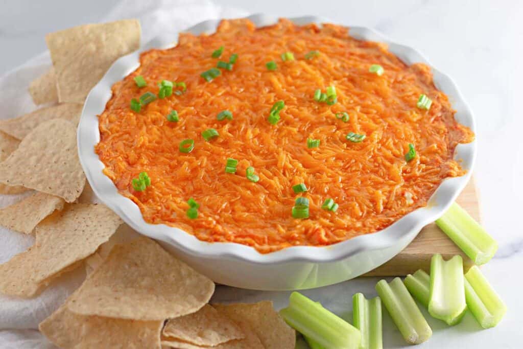 easy buffalo chicken dip in white baking dish with chips and celery