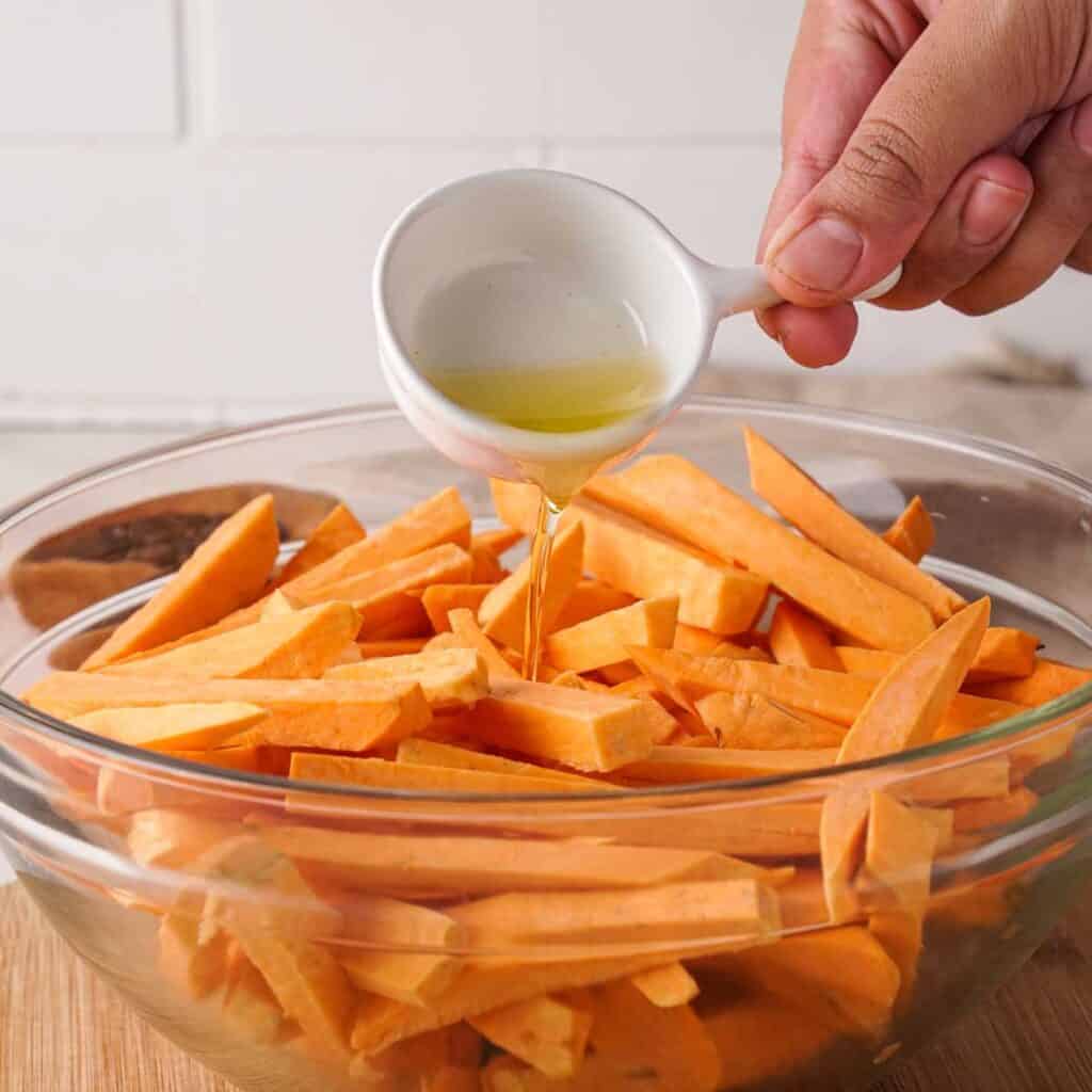 pouring olive oil on chopped sweet potato fries