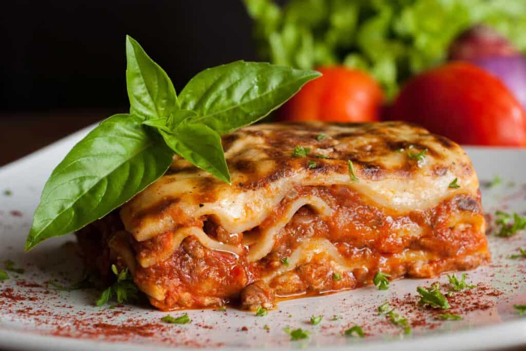 Plakje lasagne op bord gegarneerd met takje basilicum