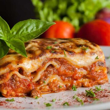 piece of lasagna on plate with basil and tomato