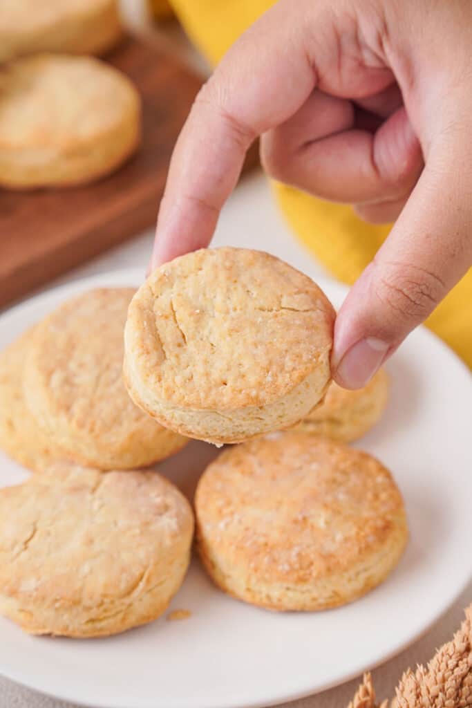 hand holding buttermilk biscuit over plate of biscuits