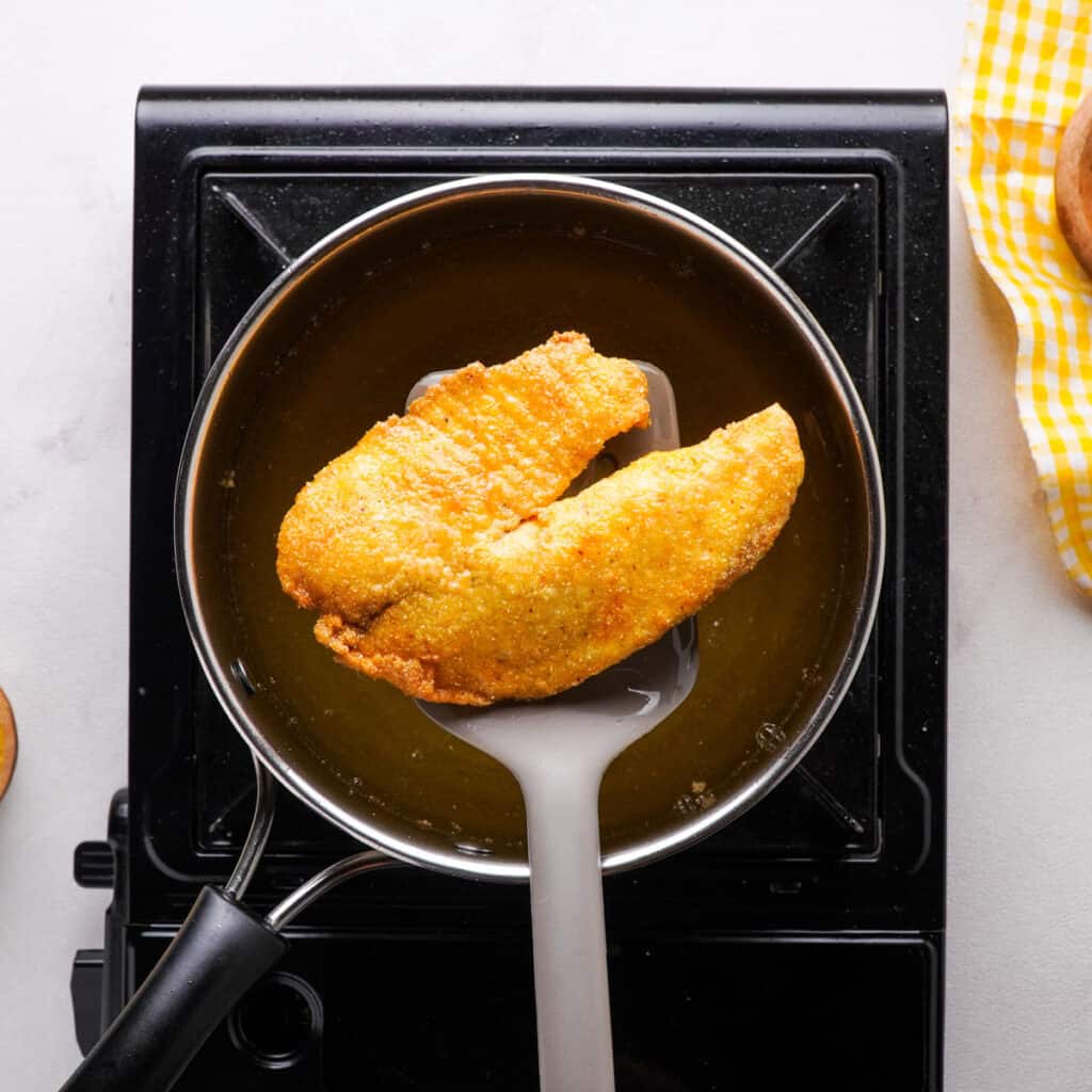 spatula removing fried catfish from frying oil