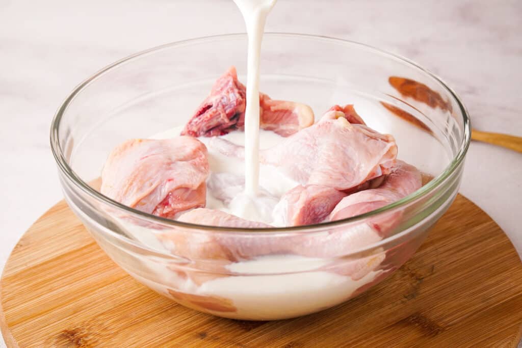 pouring buttermilk over raw chicken pieces for fried chicken