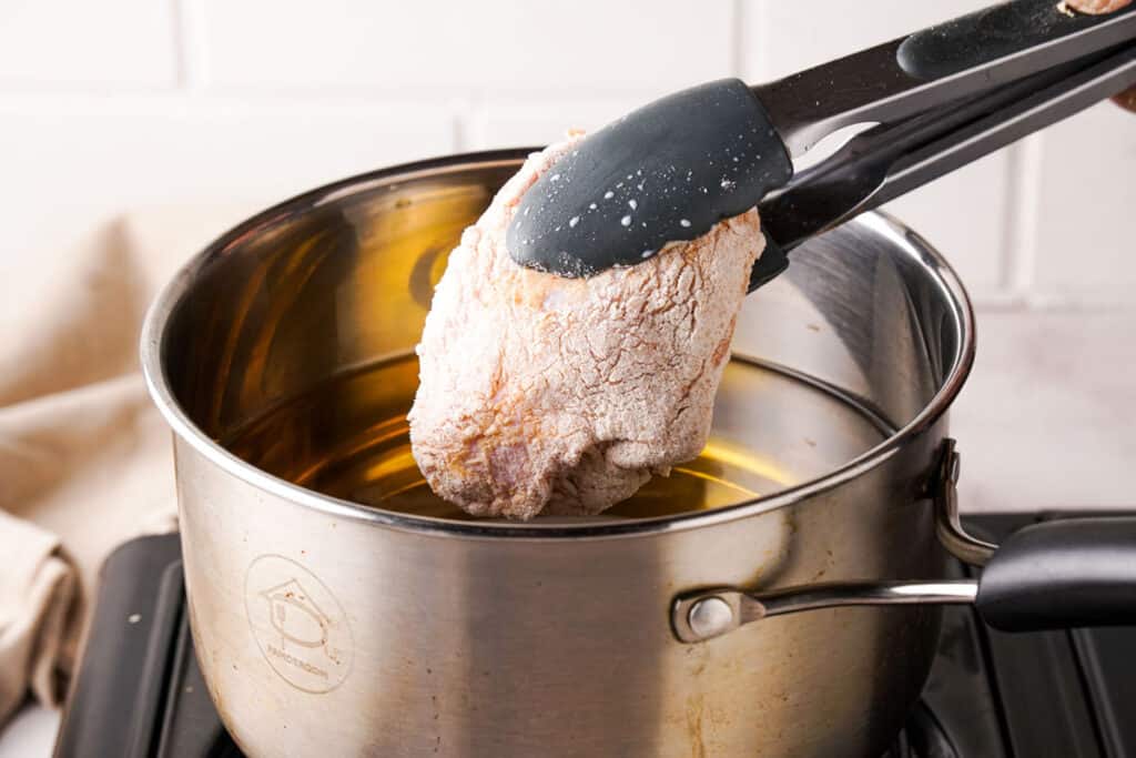 placing breaded chicken breast in oil for frying