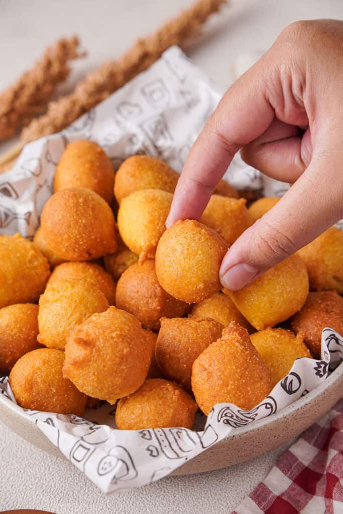 hand holding hush puppy over basket of hush puppies
