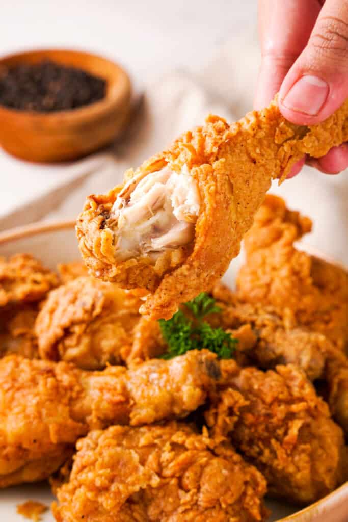 hand holding fried chicken drumstick with bite taken out