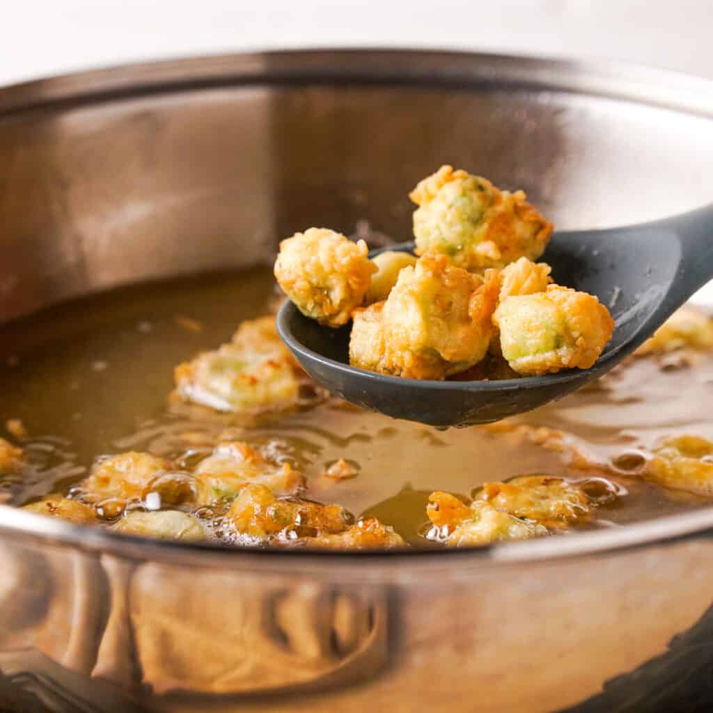 spoon removing fried okra from skillet of oil