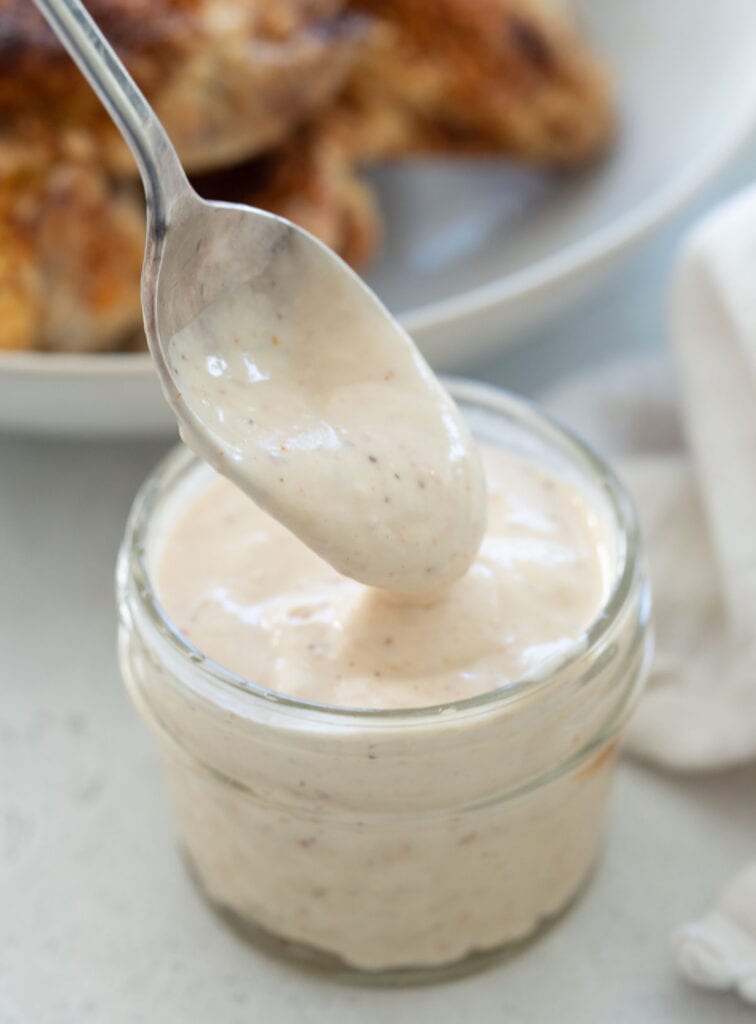 spoon dripping alabama white sauce into jar