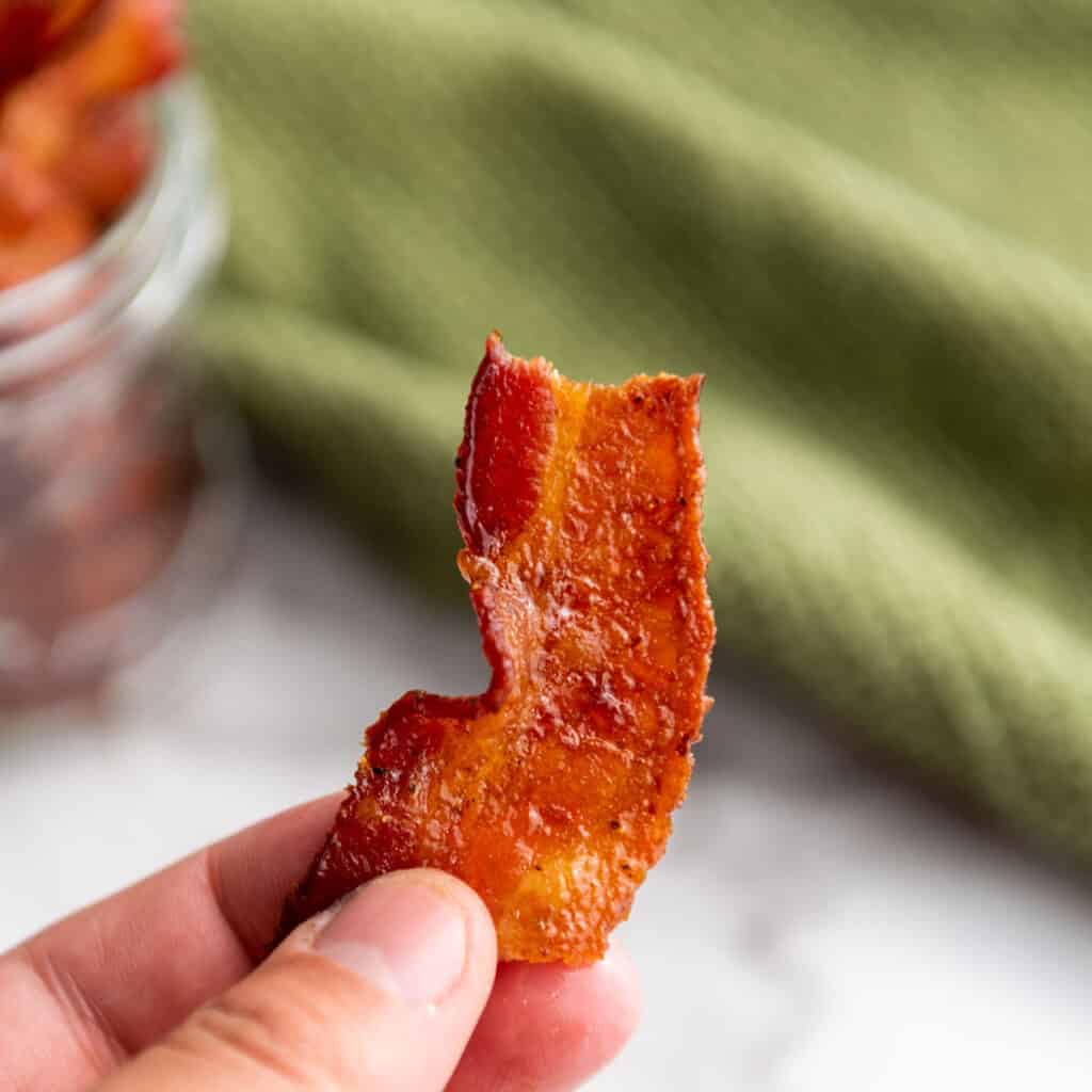 hand holding piece of candied bacon