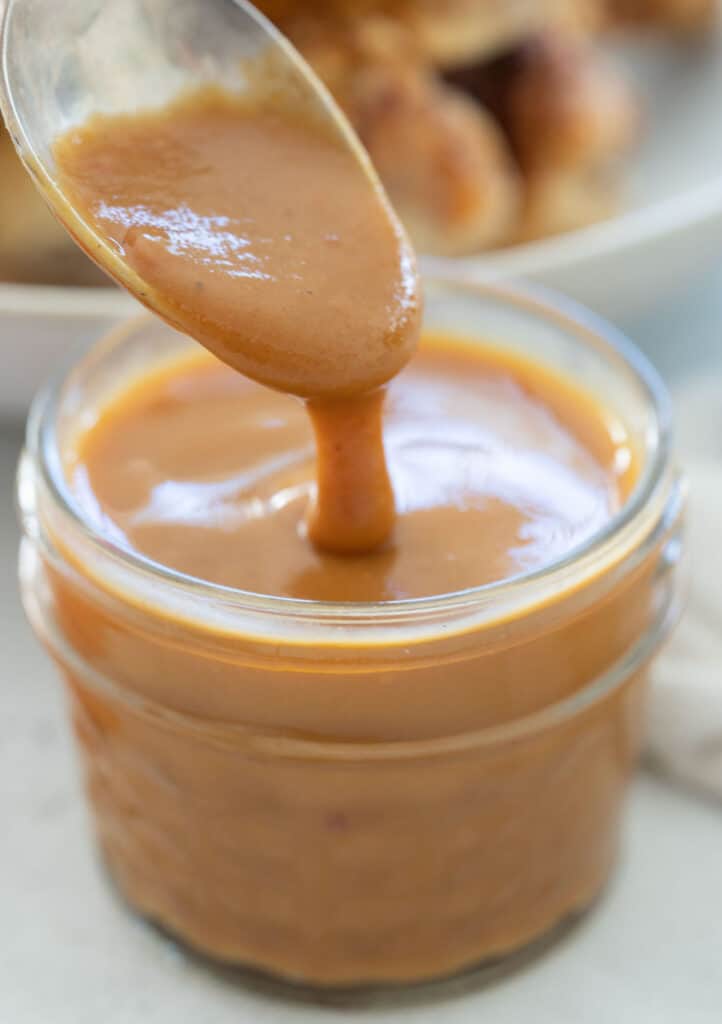 spoon dripping Carolina gold BBQ sauce into a small jar