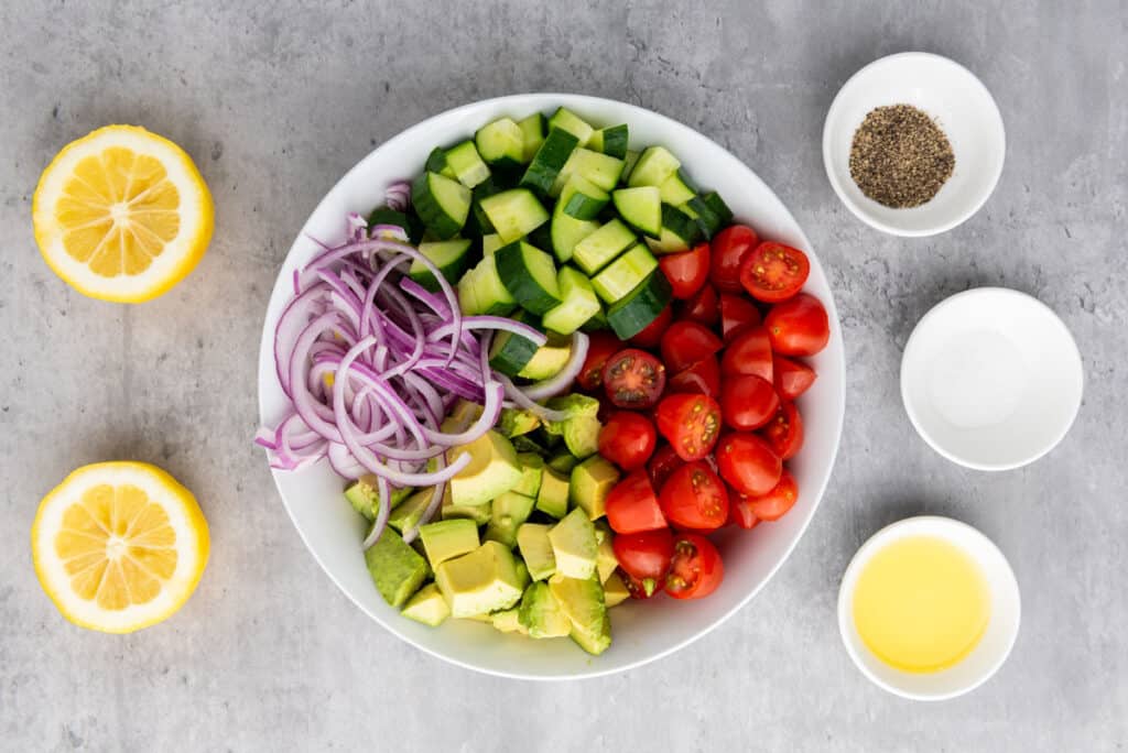 cucumber tomato avocado salad ingredients in bowl and on countertop