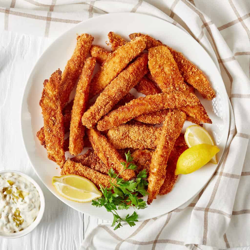 fish sticks on a white plate with lemon wedge