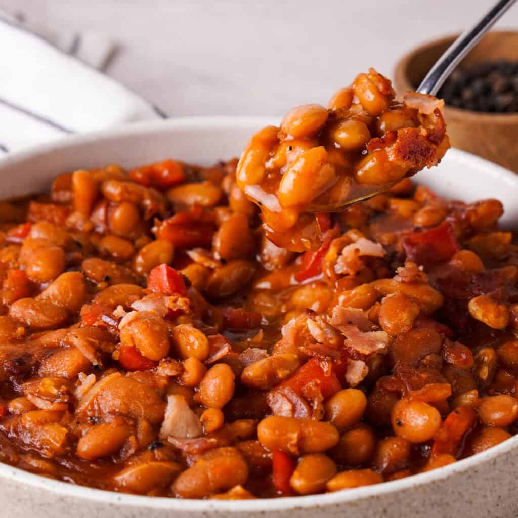 spoon scooping homemade baked beans from bowl