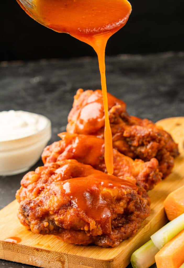 pouring buffalo sauce over chicken wings
