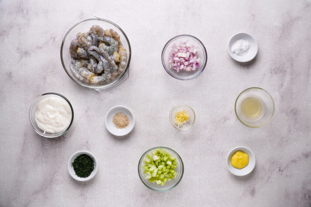 Shrimp salad ingredients in glass bowls on counter