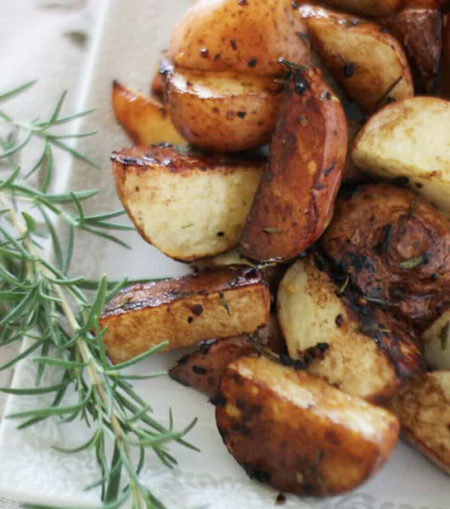 balsamic roasted potatoes on white plate with rosemary sprig