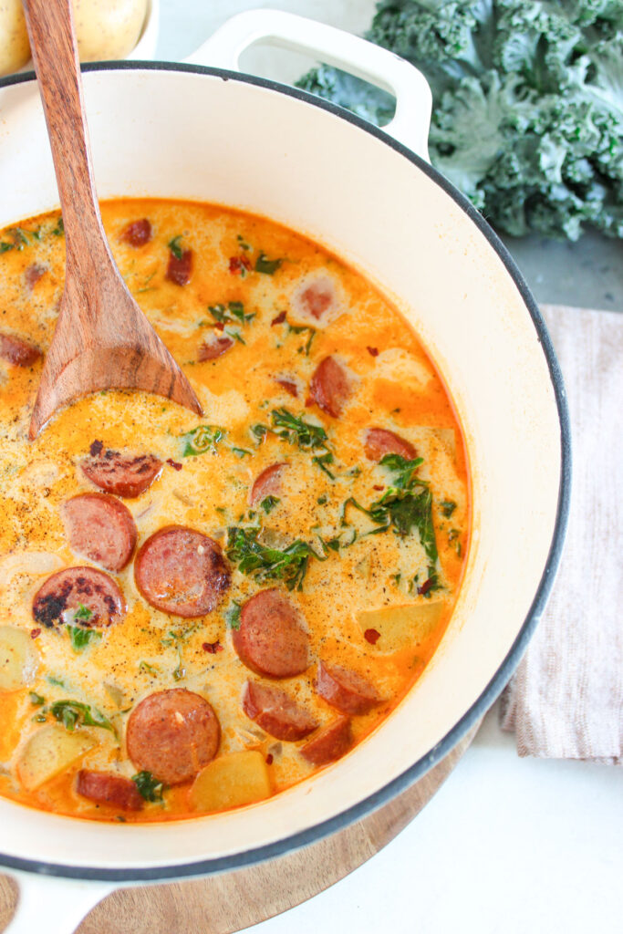 sausage potato kale soup in dutch oven with wooden spoon