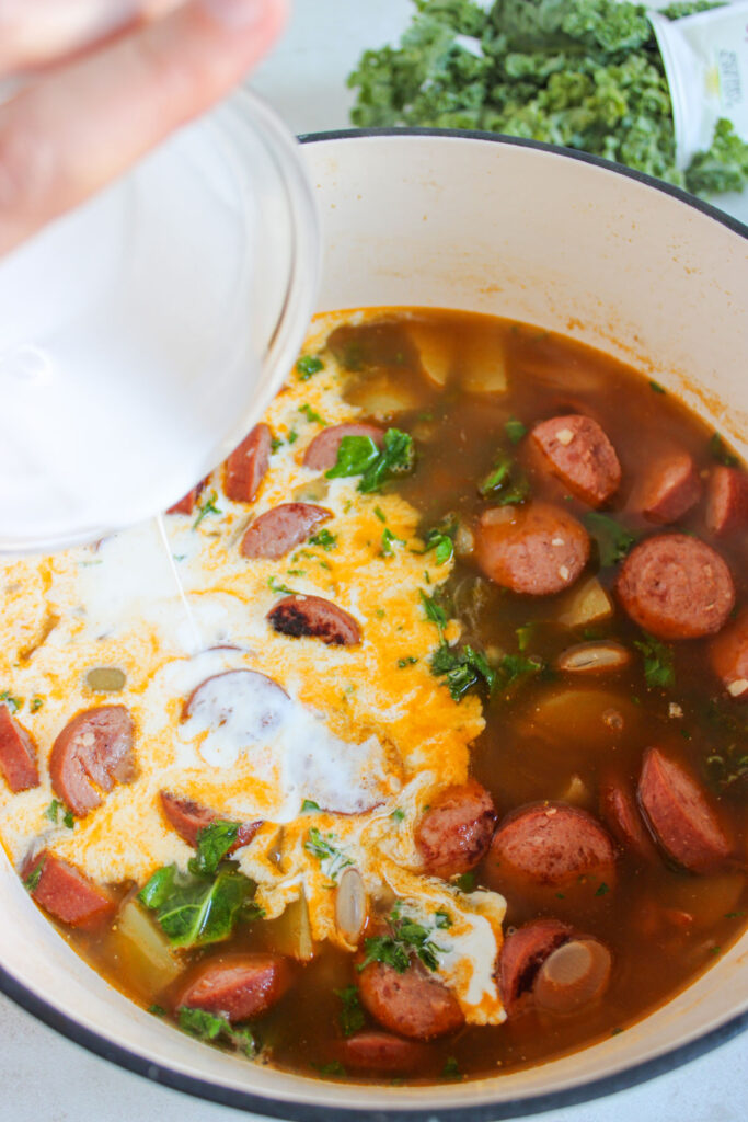 pouring cream into sausage potato kale soup