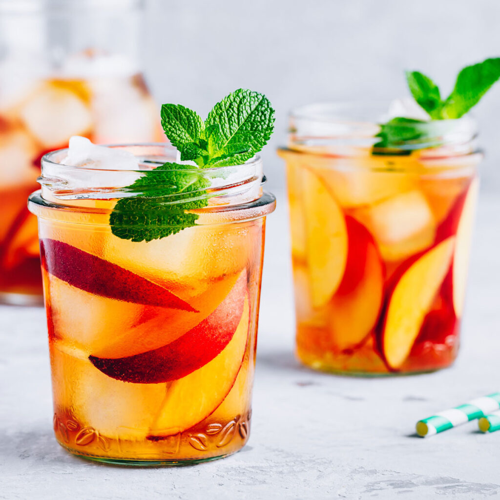 two mason jars of peach iced tea with mint sprigs