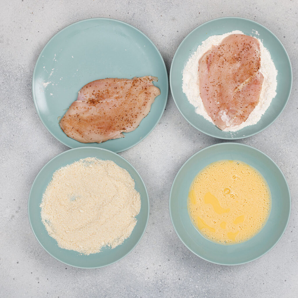 chicken breasts and breading ingredients on four plates