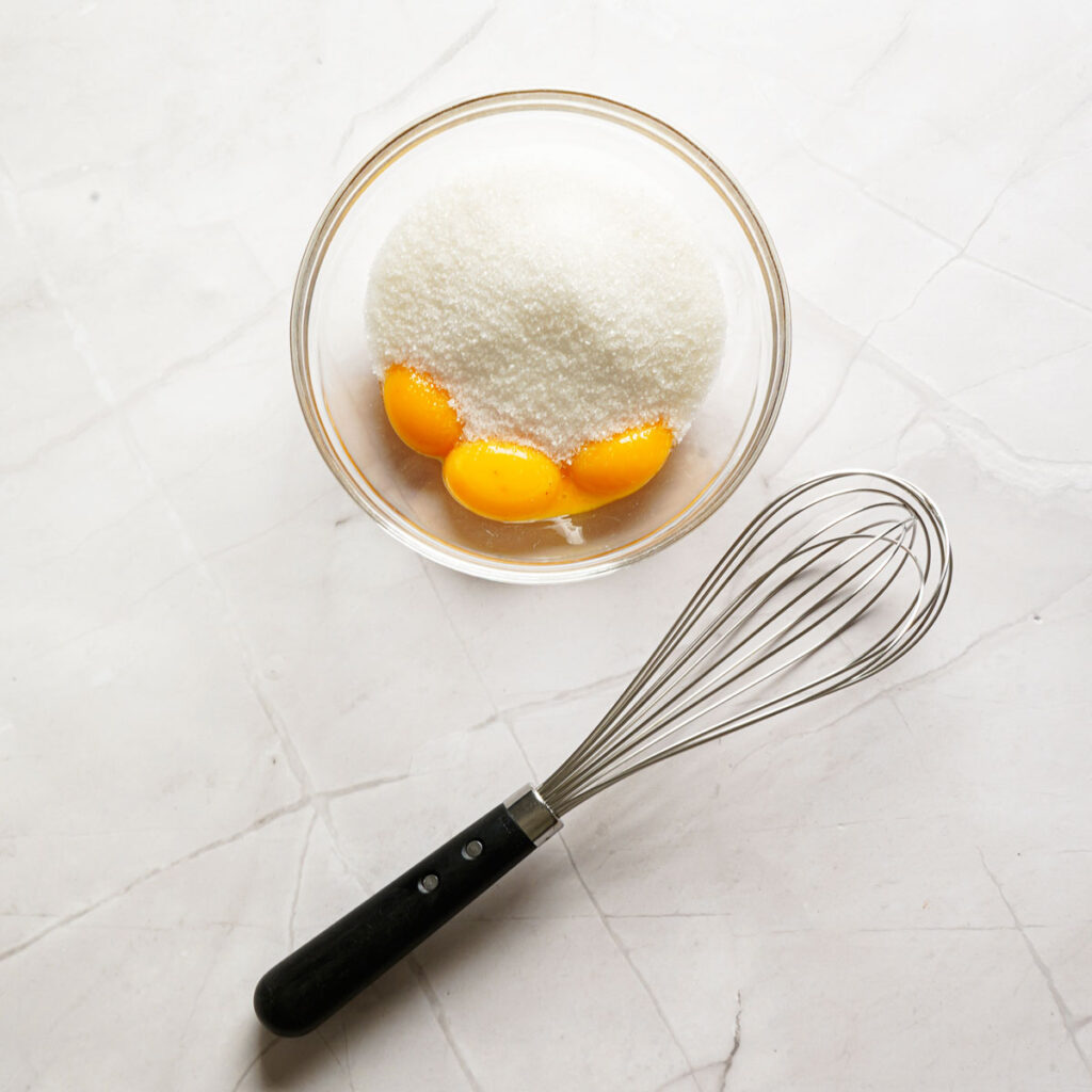 eggs and sugar in bowl with whisk nearby