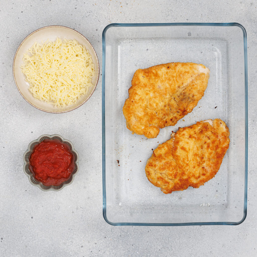 fried chicken breasts in glass dish with mozzarella and tomato paste