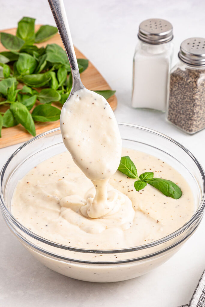 spoon dripping bechamel sauce into glass bowl