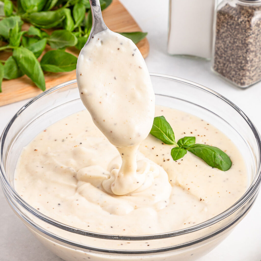 spoon dripping bechamel sauce into glass bowl