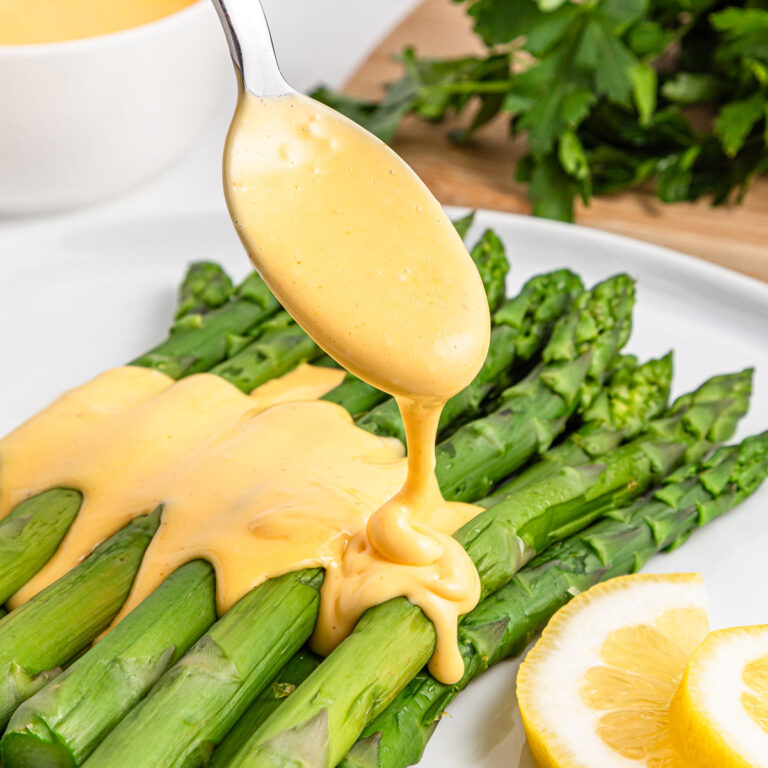 spoon pouring hollandaise sauce over asparagus