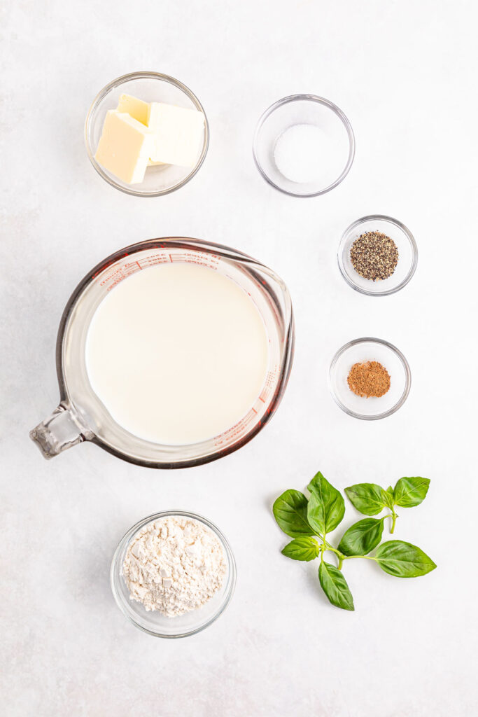 bechamel sauce ingredients in bowls on countertop with basil sprig