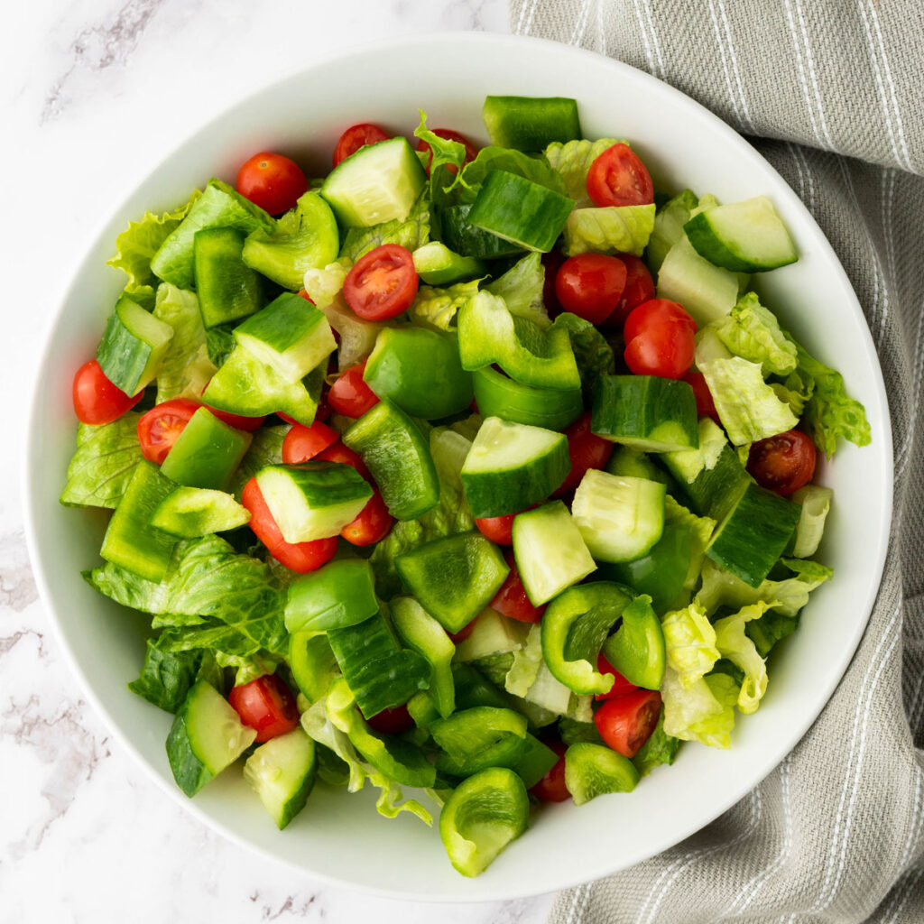 lettuce, tomatoes, and chopped cucumbers in white bowl