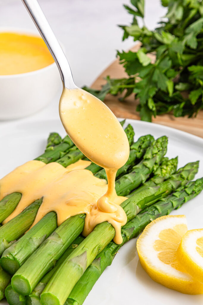 spoon pouring hollandaise sauce over asparagus
